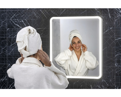 Žena s ručníkem na hlavě před osvětleným koupelnovým zrcadlem