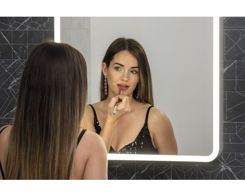 Žena se líčí rtěnkou před osvětleným zrcadlem v koupelně