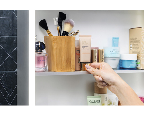 Koupelnová scéna s kosmetickými produkty, štětci na make-up a dřevěnou nádobou v zrcadlové skříňce.