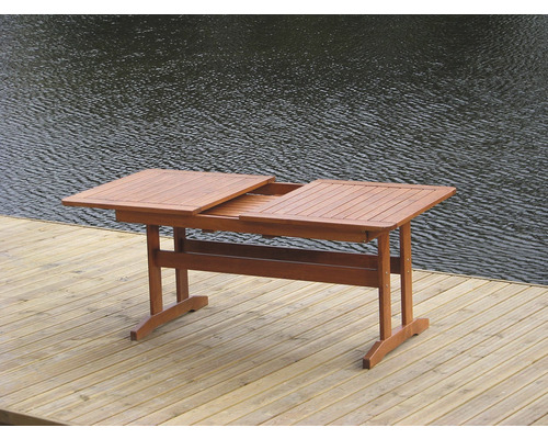 Rozkládací dřevěný zahradní stůl na dřevěné terase s vodou v pozadí.