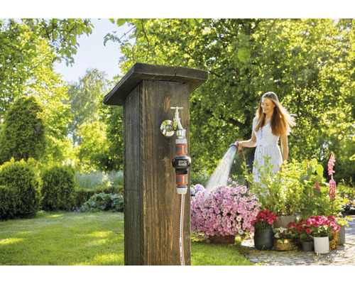 Žena zalévá květiny zahradní hadicí u kohoutku na zahradě