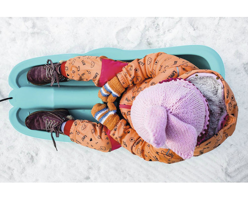 Dítě leží na saních ve sněhu.