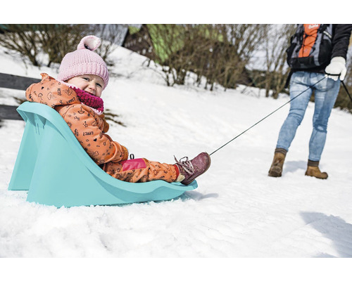 Dítě na plastových saních táhne osoba ve sněhu