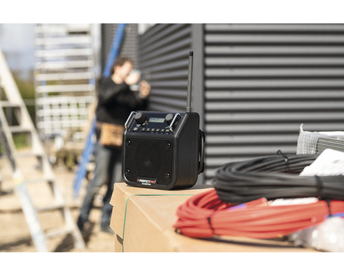 Stavební rádio s anténou a kabely a stavební dělník v pozadí