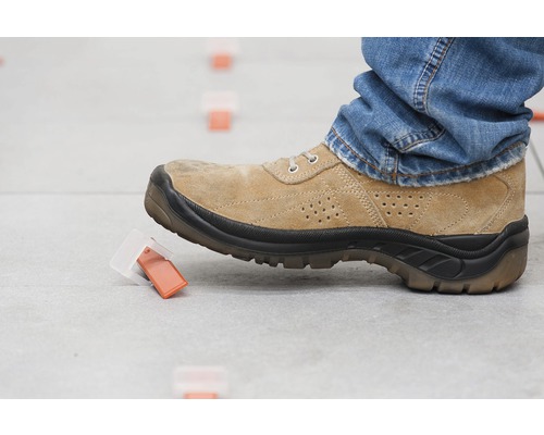 Osoba odstraňuje jazýček nivelačního systému dlaždic botou.