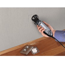 Osoba vyřezává otvor do zdi pomocí multifunkčního nástroje Dremel pro elektrickou zásuvku.