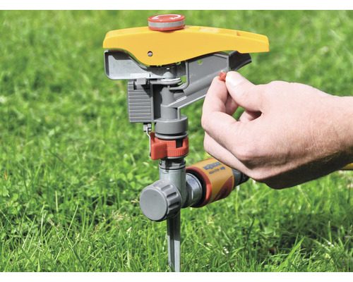 Zahradní postřikovač na trávníku s rukou nastavující zavlažování