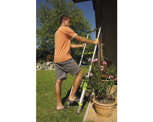 Osoba používá teleskopický žebřík na zahradě pro venkovní práce.