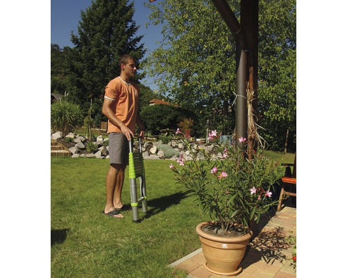 Muž drží teleskopický žebřík na zahradě.