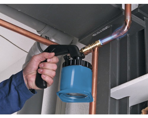 Řemeslník pájí měděné trubky pomocí pájecí lampy.