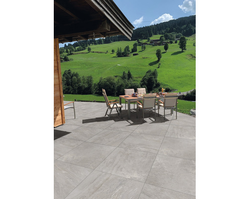 Keramická dlažba 60x120x2 cm Alpen grigio Terasa se zahradním stolem a židlemi před zelenou krajinou.