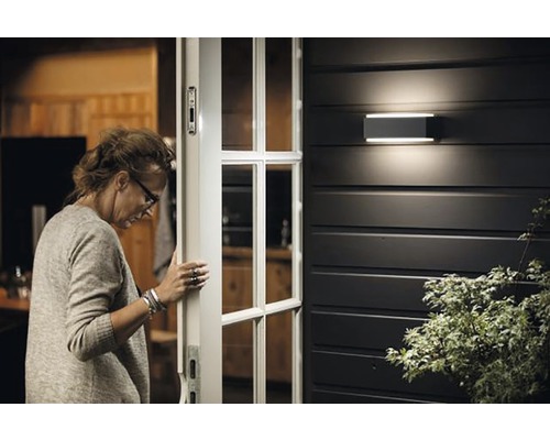 Žena otevírá vchodové dveře s venkovní nástěnnou lampou