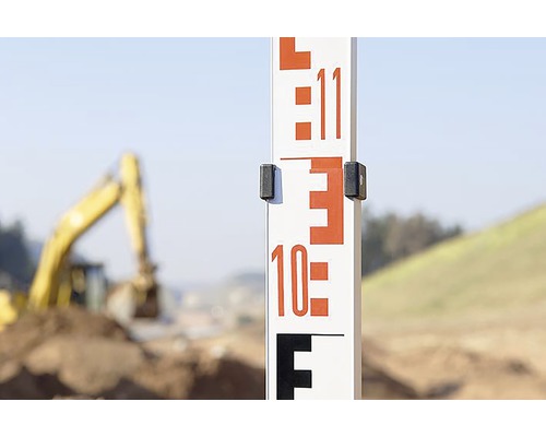 Nivelační lať na staveništi s bagrem v pozadí