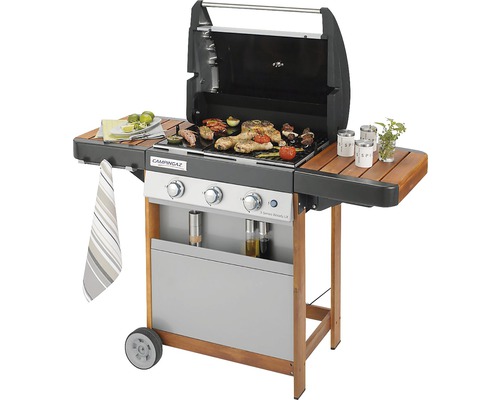 Plynový gril s jídlem na grilovací mřížce a bočními policemi.