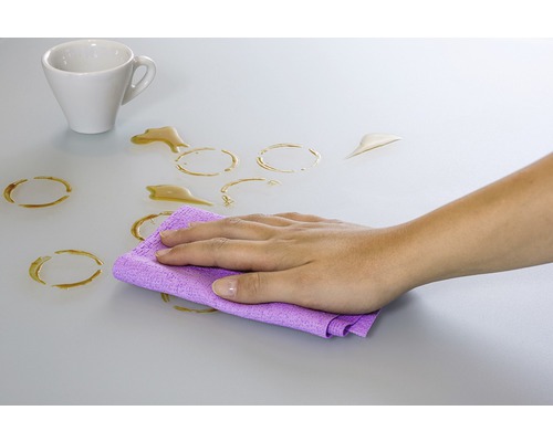 Ruka utírá hadříkem skvrny od kávy ze stolu.