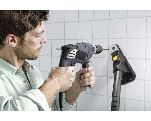 Muž vrtá díru do obkládané stěny s vrtačkou vedle vysavače