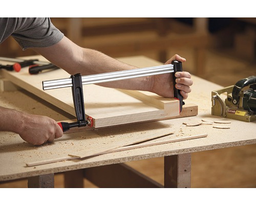 Osoba používá svěrku k upevnění kusů dřeva na pracovní stůl.