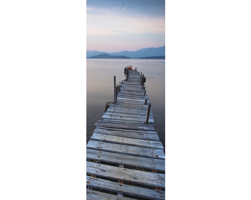 Dlouhé staré dřevěné molo vede do vodní plochy s horami v pozadí.