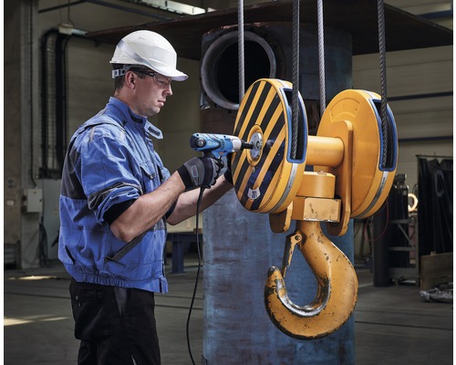 Muž s vrtačkou na jeřábovém háku v dílně