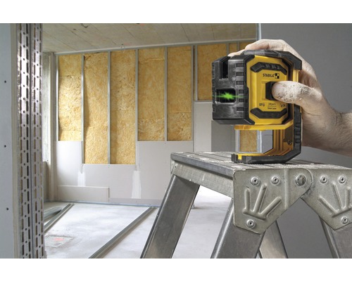 Logo společnosti Stabila. Řemeslník obsluhuje žlutý a černý čárový laser na žebříku v místnosti se stěnovou izolací.