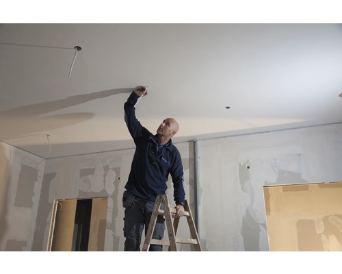 Muž na žebříku provádí elektroinstalace v interiéru.