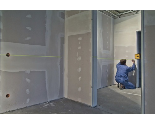 Řemeslník používá laserový dálkoměr v místnosti se sádrokartonovými stěnami k provádění měření.