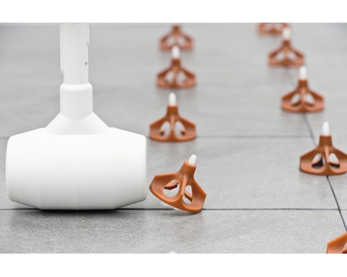 Systém vyrovnávání dlaždic s kladivem, klíny a tahacími jazýčky na dlaždicové podlaze