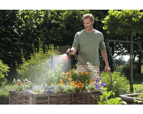 Muž zavlažuje květiny ve vyvýšeném záhonu zahradní hadicí