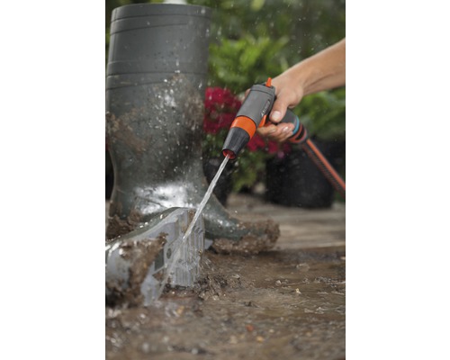 Osoba čistí zahradní lopatu zahradní sprchou vedle gumáků.