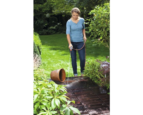 Žena zalévá hadicí terasu a květinovou vázu na zahradě.