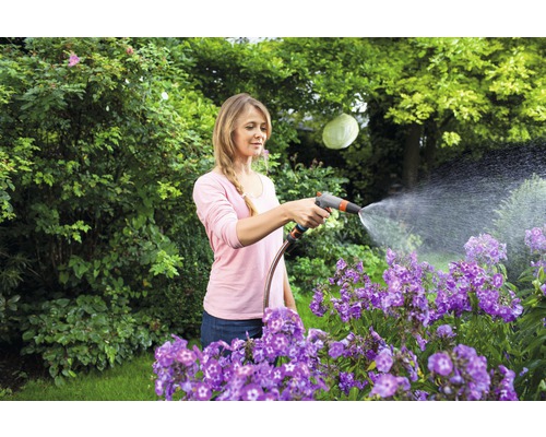 Žena zalévá květiny zahradní hadicí na zahradě.