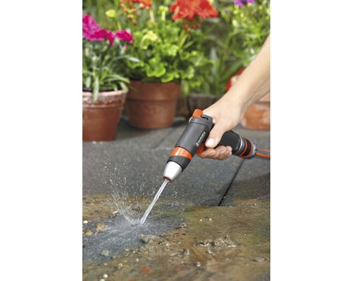 Osoba používá zahradní stříkací pistoli k čištění terasy před osázenými květináči.