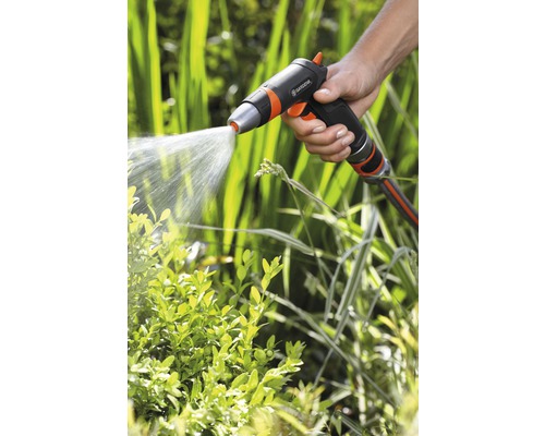 Ruka drží zahradní postřikovač, který stříká vodu na rostliny.