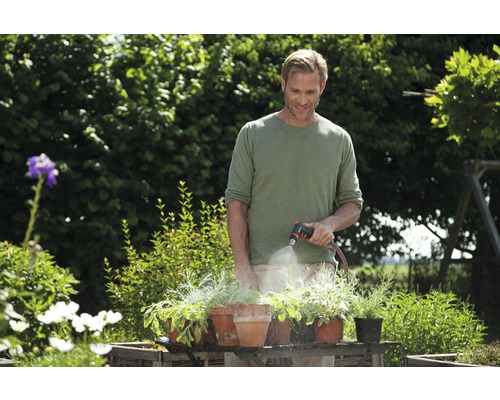 Muž zalévá rostliny v květináčích zahradní hadicí na zahradě.