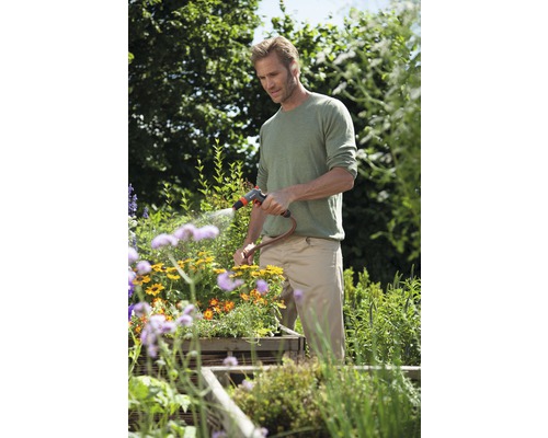 Muž zavlažuje květiny zahradní hadicí na zahradě.