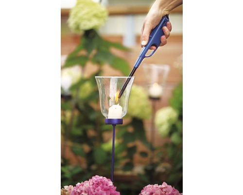 Ruka zapaluje svíčku ve svícnu pomocí zapalovače.