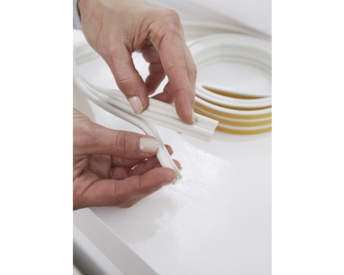 Ruce drží bílou ozdobnou lištu s lepicí páskou