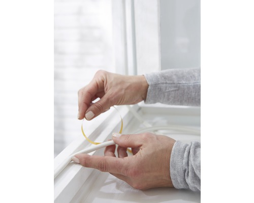 Osoba připevňuje těsnicí pásku na okenní rám.