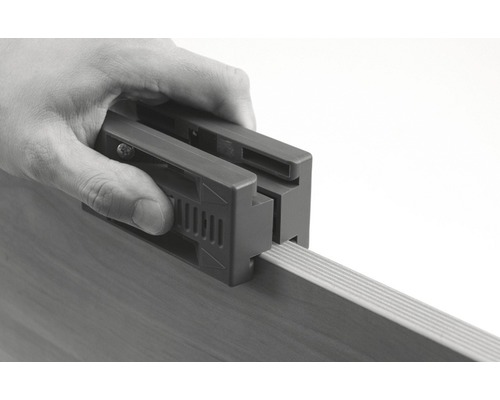 Osoba používá lepicí pomůcku k připevnění hranové pásky k dřevěné desce.