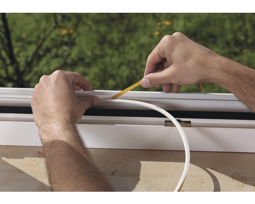 Osoba upevňuje těsnicí pásku na okenní rám.