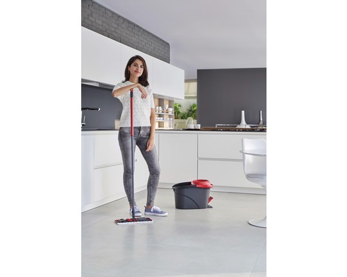 Žena se opírá o mop vedle kbelíku ve světlé kuchyni.