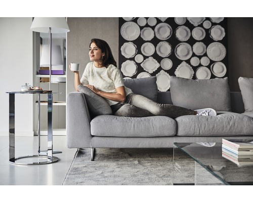 Žena relaxuje na šedé pohovce v obývacím pokoji s moderním dekorem.