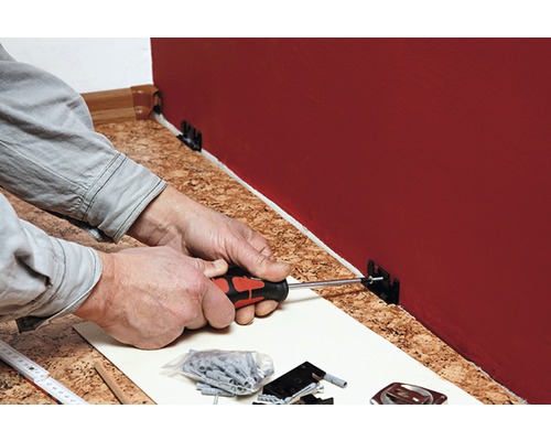 Osoba montuje soklovou lištu pomocí šroubováku