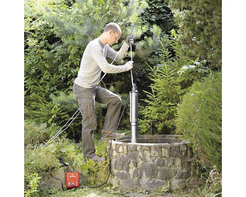Muž instaluje hlubinné čerpadlo do studny v zahradě.