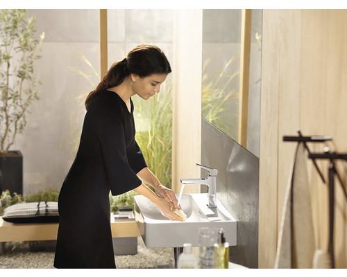 Žena si myje ruce v moderní koupelně s umyvadlem na desku a vodovodní baterií.