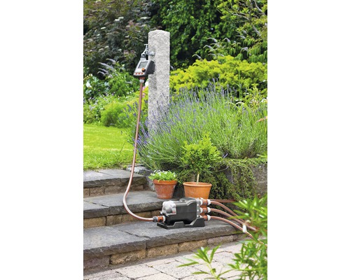 Zahradní zavlažovací systém s zavlažovacím počítačem, rozdělovačem a zavlažovacími hadicemi na zahradě