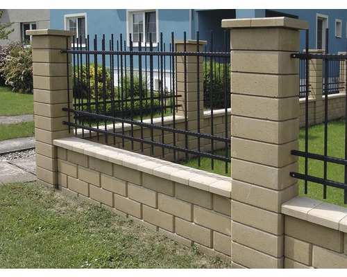 Ozdobná zahradní zeď s betonovými ozdobnými prvky a černým kovovým plotem.