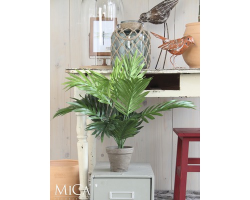 Dekorativní umělá rostlina v květináči na příručním stolku, obklopená dalšími dekorativními prvky.