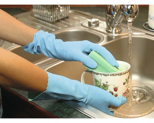 Ruce s mycími rukavicemi umývají šálek houbou pod tekoucí vodou v umyvadle.