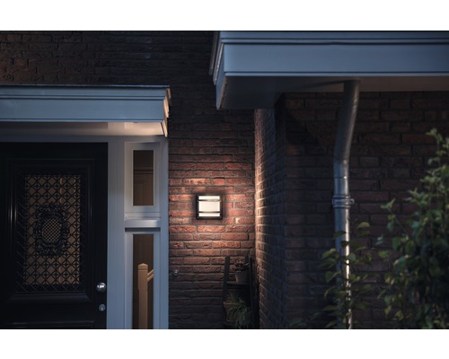 Osvětlená stěna domu s obdélníkovým venkovním svítidlem vedle vchodových dveří